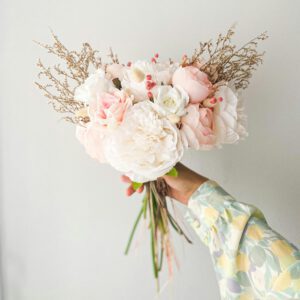 Ein weißer Brautstrauß der mittig von einer Frau gezeigt wird